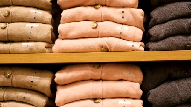 Stack of folded sweaters on shelf in store close-up front view.