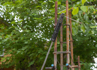 A welding torch hanging from the armature column - construction concept. Green nature background