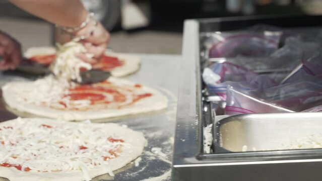 Close up, woman's hands spreading mozzarella cheese on fresh pizza dough in slow motion