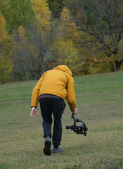 man in yellow jacket shoots documentary with video stabilizer in nature.