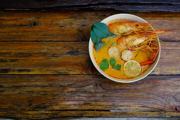 Fototapeta na wymiar Tom yum kung in a cup on a wooden floor, Tom yum kung is also the national dish of Thailand. And is a food that is famous all over the world.