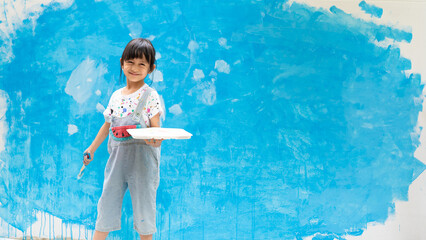 Banner of cute 5 years old asian little girl is smiling while painting the wall with water color at home, concept of art education for kid, homeschooling and learning activity by playing for child.