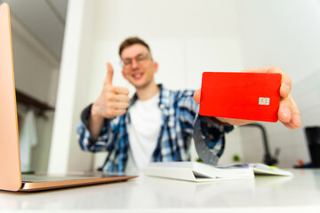 A man in a plaid shirt and glasses smiles and holds a credit card in his hands. A bank card in the...