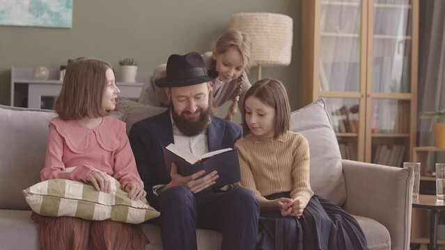 Jewish man reading the Tanakh to his three daughters on Hanukkah, celebrating at home
