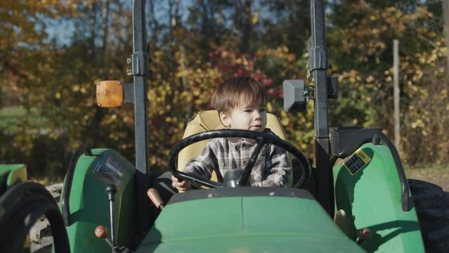 Asian kid playing behind the wheel of an old tractor on a farm. Front view