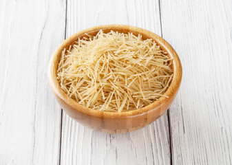 Uncooked filini pasta in wooden bowl on white wooden background