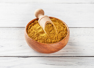 Curry powder in wooden bowl with scoop on white wooden background