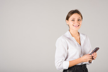 Fototapeta premium A businesswoman uses a mobile phone on a gray background with a copy space for advertising.