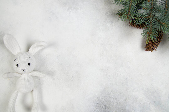 A white knitted bunny, spruce branches on a gray background. Christmas background.