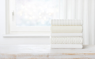 Folded sweater stack on table over blurred window with space