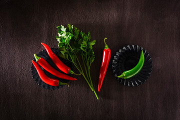 Red hot chili peppers on saucers and parsley greens on a black wooden background.