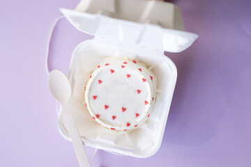 A small bento cake in eco packaging with a wooden spoon on a purple background