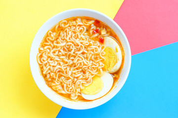 Ramen noodles with eggs in a bowl close-up on yellow, blue and red background, top view.