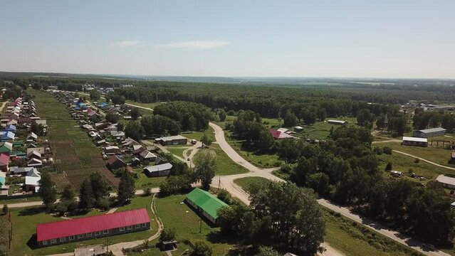 Aerial shot of flight forward over the village, gardens and some trees. Countryside road with moving car. Sunny summer and some light clouds on the sky