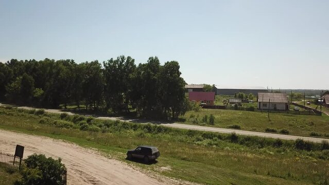 Take-off аerial shot of coutryside road with village on back when sunny summer and some light clouds. Some rural houses and forest under. Cell tower in distance