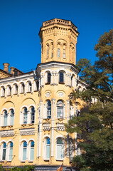 A low angle landscape view of vintage yellow brick building with the tower against blue sky. Neo-gothic style architecture