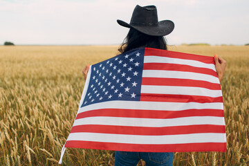 Woman farmer wearing cowboy hat, plaid shirt and jeans with american flag at wheat field