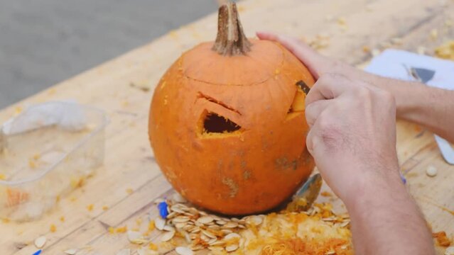 Preparing pumpkin for Halloween. The hands of an adult carve a scary figure with a pumpkin.