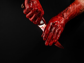A man wipes a bloody knife with his hand on a black background. 