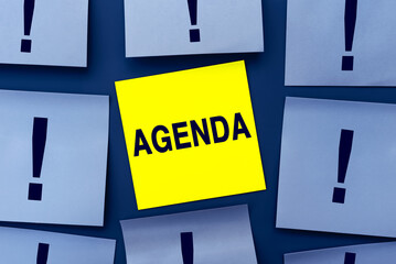 Obraz premium Yellow sticky sticker with text AGENDA of attention among blue note papers. Business concept. Home Office