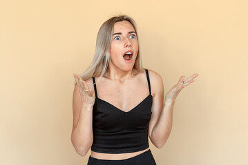 Surprised young woman with amazement face and open-mouthed. Shocked girl looking aside. Indoor studio shot on beige background