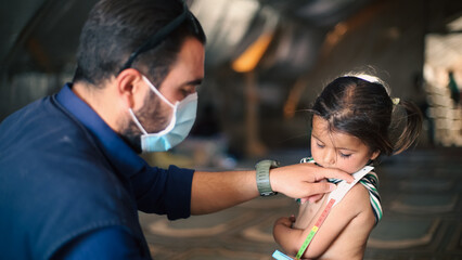 A doctor examines children's malnutrition inside a refugee camp. Malnutrition was measured using a mid-upper arm circumference belt.  - obrazy, fototapety, plakaty