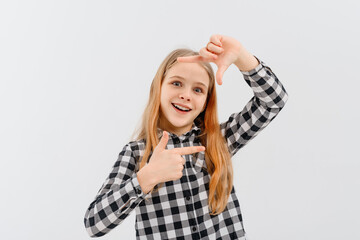 Young beautiful teen girl with blonde hair wearing casual plaid shirt, stands over white studio background, smiling making frame with hands and fingers with happy face