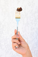Chocolate candy with nuts on a fork over white background. Tender female hand holding a fork with candy. Vertical photo