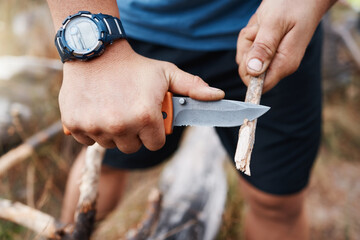 Hands, knife and cutting with a hiking man carving a stick outdoor in nature while camping for...