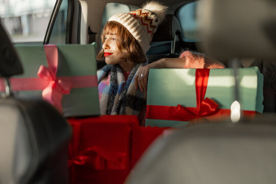 Young woman dressed for the holidays drives in car on back seat with beautifully wrapped Christmas presents. In anticipation of the winter holidays, preparation and shopping