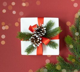 A white gift box with a red ribbon, cones and fir branches on a white background. Top view.