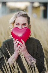 thoughtful young woman hoping or searching for self love and holding a red heart air balloon...