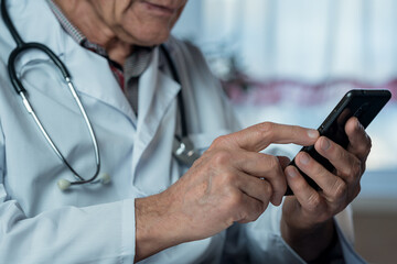 Mature doctor in white uniform holding smartphone in hands close up side view