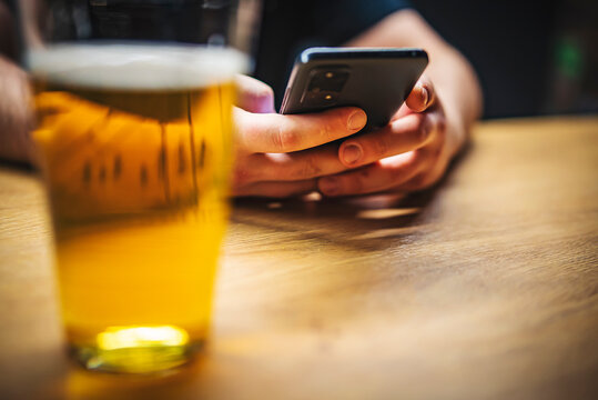 close up of man hand hold smartphone, drinking beer and reading message at bar or pub