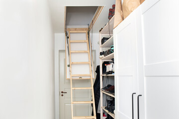 Wooden ceiling pull down attic folding stairs in small minimalist hallway corridor, space saving in home concept.