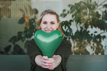 smiling young vegan girl full of joy holding a green heart air balloon in her hand for more environmentally friendly awareness to care about planet earth against climate change 