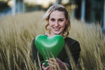 positive thinking young woman full of joy & self love holding a green heart air balloon in her hand...