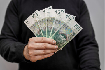 A man holding Polish banknotes in a fan of PLN 100. Financial concept 500 plus - Bills, debts, current financial problems in the world.	
