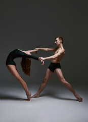 The two beautiful young contemporary dance couple. Emotional duet performing choreographic art  isolated in dark grey background. Modern ballet lift. Studio photo. Concept of art, style, fashion. - obrazy, fototapety, plakaty