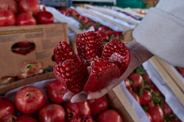 A woman holds an open pomegranate in her hand. A woman chooses a pomegranate from a cardboard box in the market. The girl holds a ripe pomegranate cut into pieces. Selective focus.