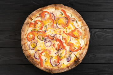 Hot tasty traditional Italian pizza with red onion, pepper, cheese on a dark wood background. Top view