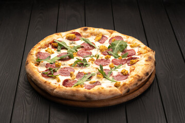 Classic Italian meat pizza with salami, cheese, arugula on a plate. Black background. Italian cuisine, selective focus