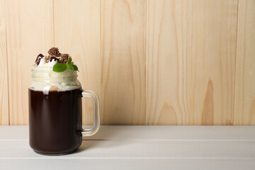 Mason jar of delicious hot chocolate with whipped cream and mint on white wooden table. Space for...