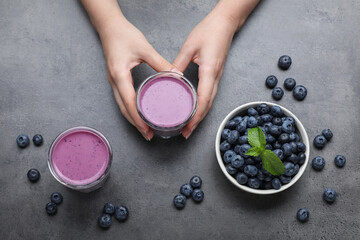 Woman with tasty blueberry smoothie at grey table, top view