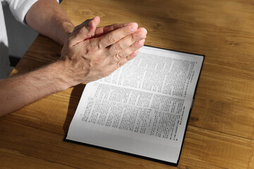Naklejka premium Man with Bible praying at wooden table, closeup