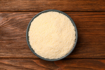 Delicious grated parmesan cheese in bowl on wooden table, top view
