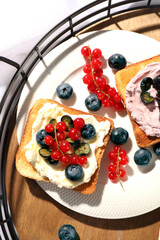 Sandwiches with cream cheese and berries on wooden tray, flat lay
