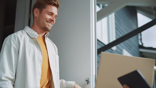Close Up Portrait of a Handsome Homeowner Receiving a Parcel from a Happy Young Mailman. Postal Service Worker Comes to the House to Make a Delivery and Get a POD Signature on Tablet Computer.