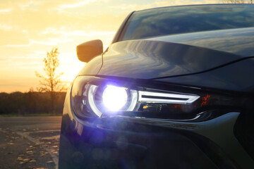 Black modern car parked on road at sunset, closeup of headlight