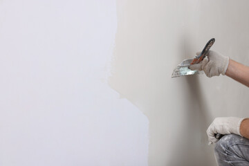Worker plastering wall with putty knife indoors, closeup. Space for text